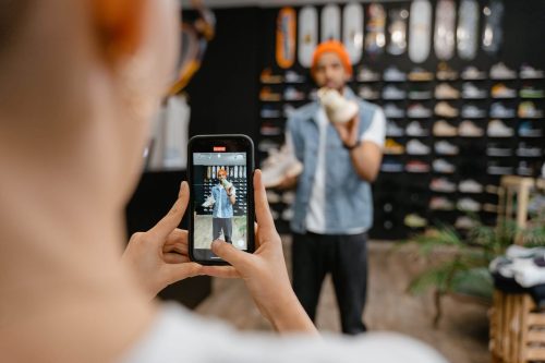 un joven haciendo un video para tiktok con par de zapatos en la mano, hay otro joven grabando.